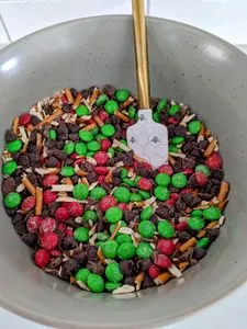 A large mixing bowl with red and green M&Ms, chocolate chip, chunks, and pretzel mixture. (opens in a new tab)